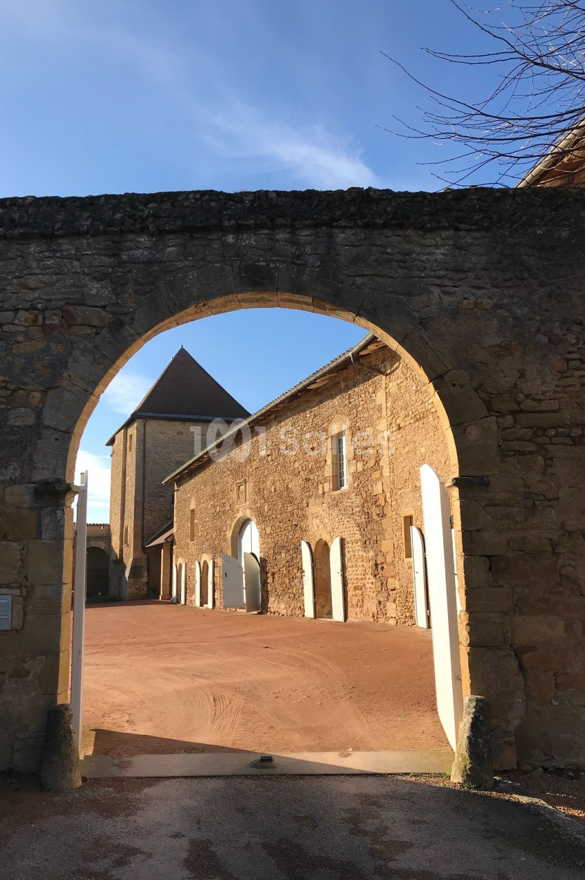 Vue d'une cour intérieure ensoleillée avec des bâtiments en pierre et une arche en premier plan.