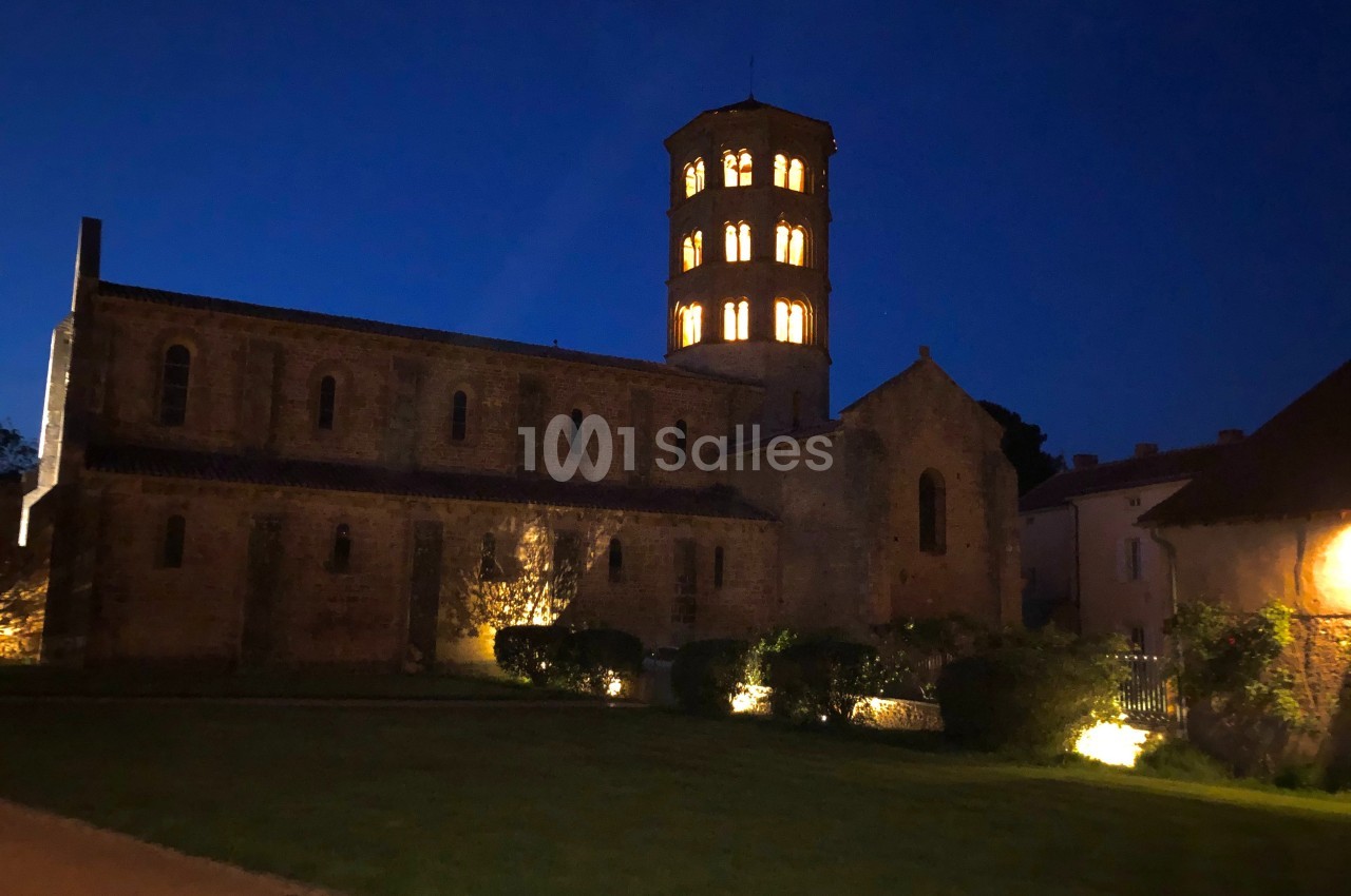 Église en pierre éclairée la nuit, avec un clocher illuminé et un jardin à l'avant.