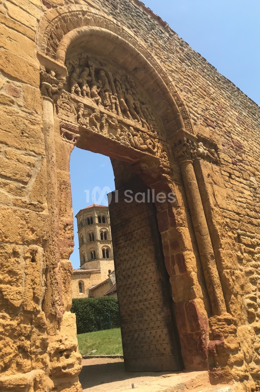 Vue d'une porte en pierre sculptée donnant sur une tour romane sous un ciel bleu.