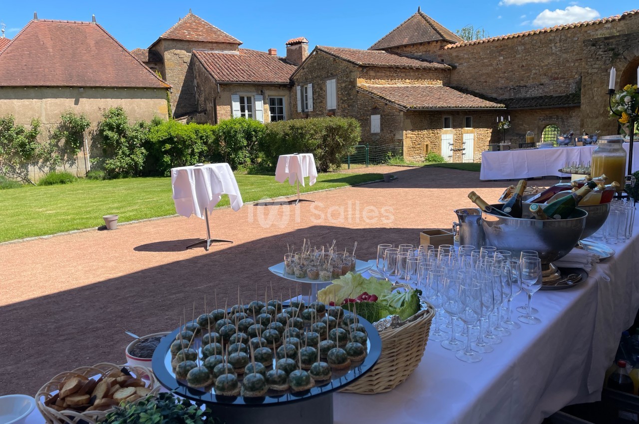 Table dressée pour un buffet en extérieur avec verrines, amuse-bouches et boissons, dans une cour ensoleillée.