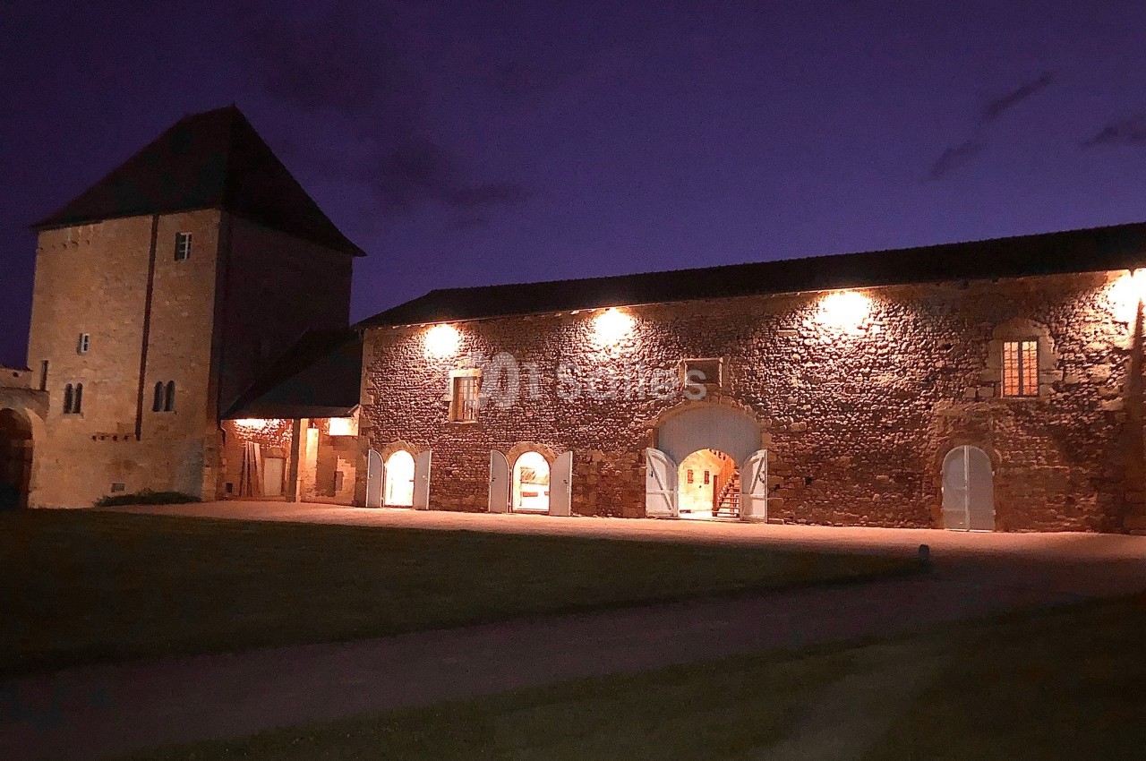 Bâtiment en pierre éclairé la nuit, avec une grande porte voûtée et des fenêtres illuminées.