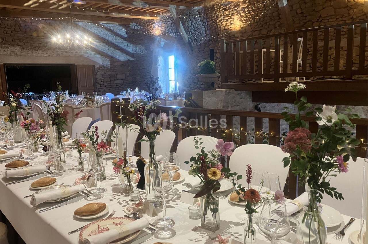 Salle de réception décorée pour un mariage, avec tables dressées, fleurs colorées et lumières chaleureuses.