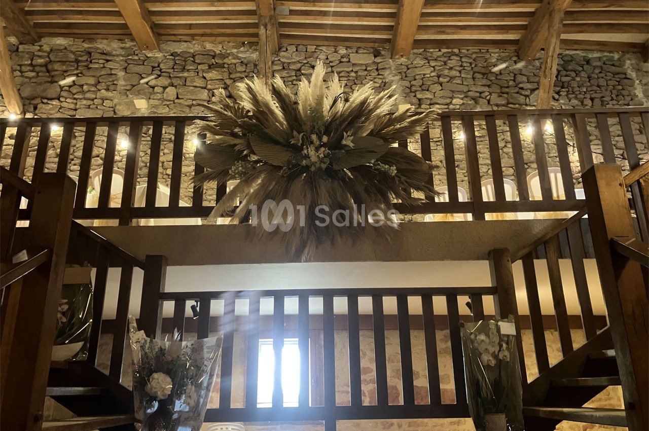 Décoration florale suspendue en pampas et feuillages dans une salle avec murs en pierre et poutres apparentes.