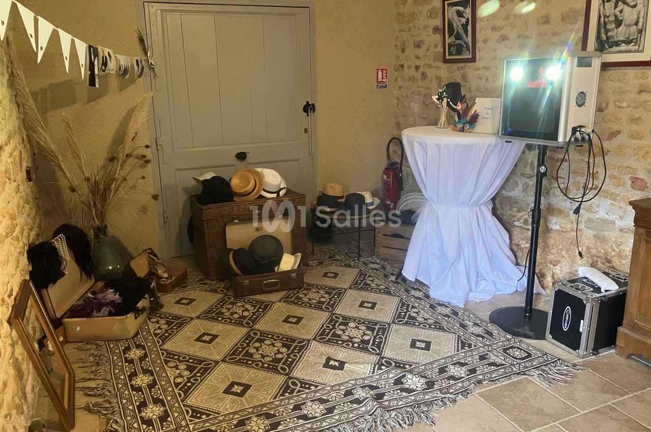 Espace décoré avec des accessoires rétro, un tapis à motifs, un photobooth et des chapeaux dans une pièce en pierre.