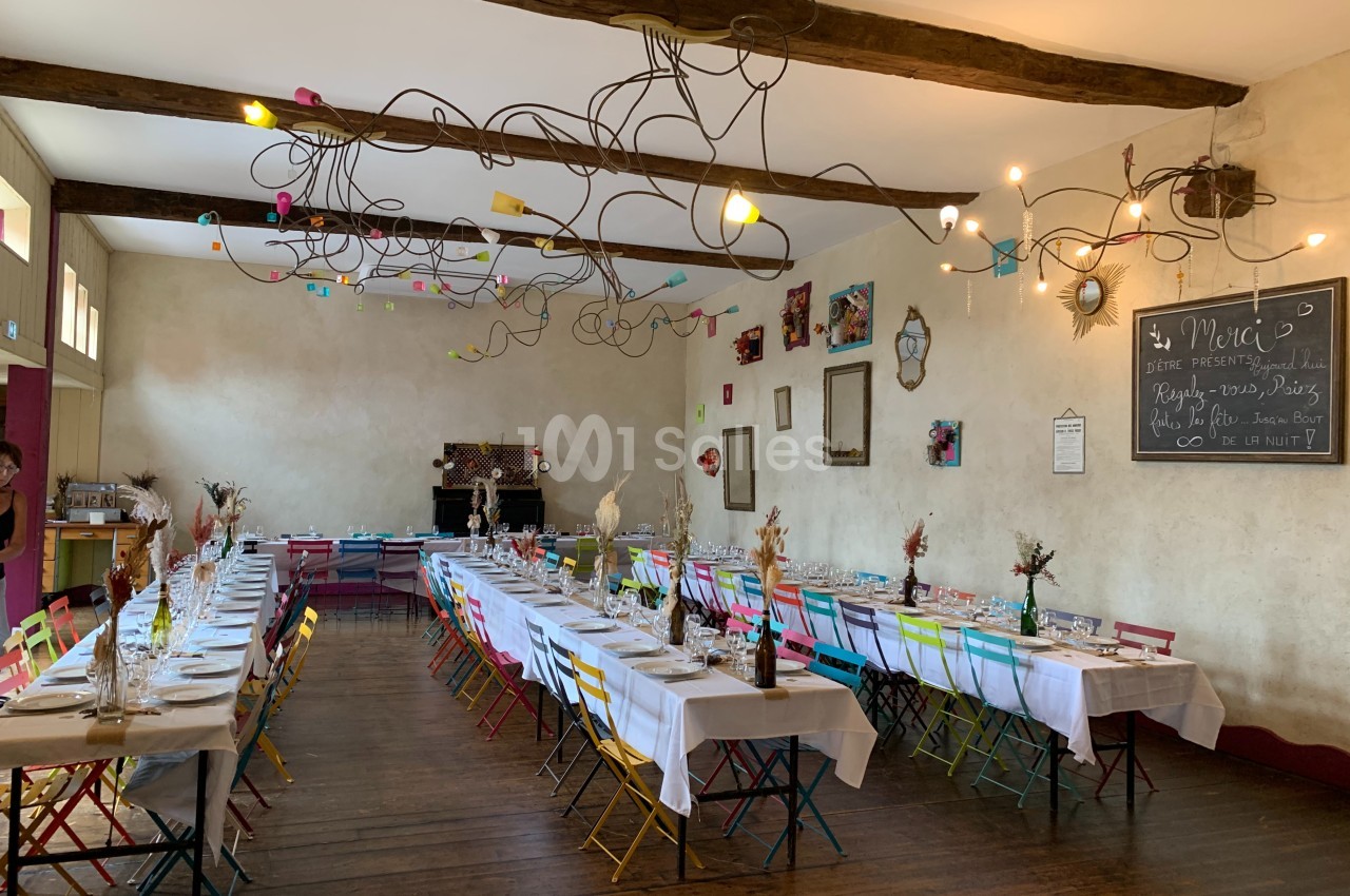 Salle de réception décorée avec des tables dressées, chaises colorées et éclairage suspendu original.