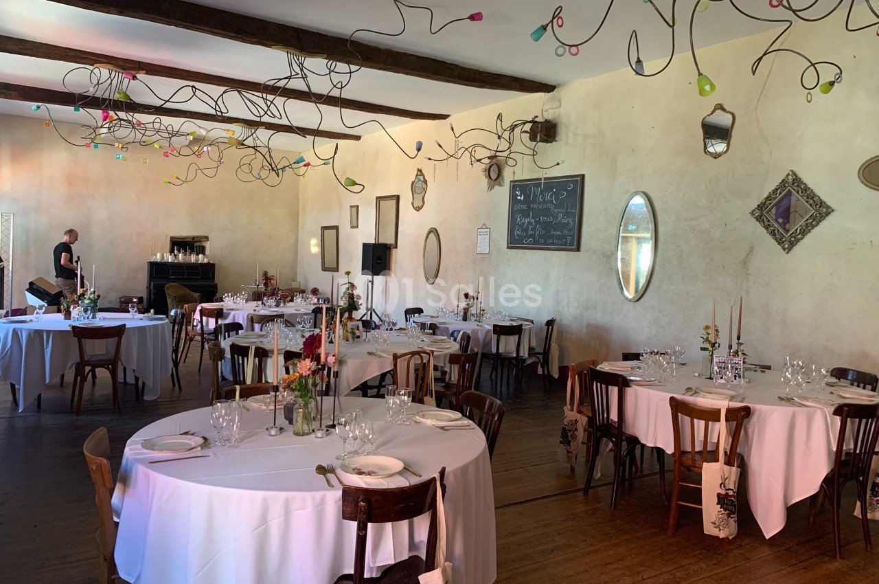 Salle de réception décorée avec des tables rondes dressées, des chaises en bois et des ornements suspendus au plafond.