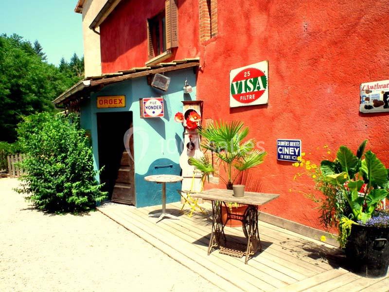 Façade colorée d'un bâtiment avec des enseignes vintage, une table en métal et des plantes sur une terrasse en bois.