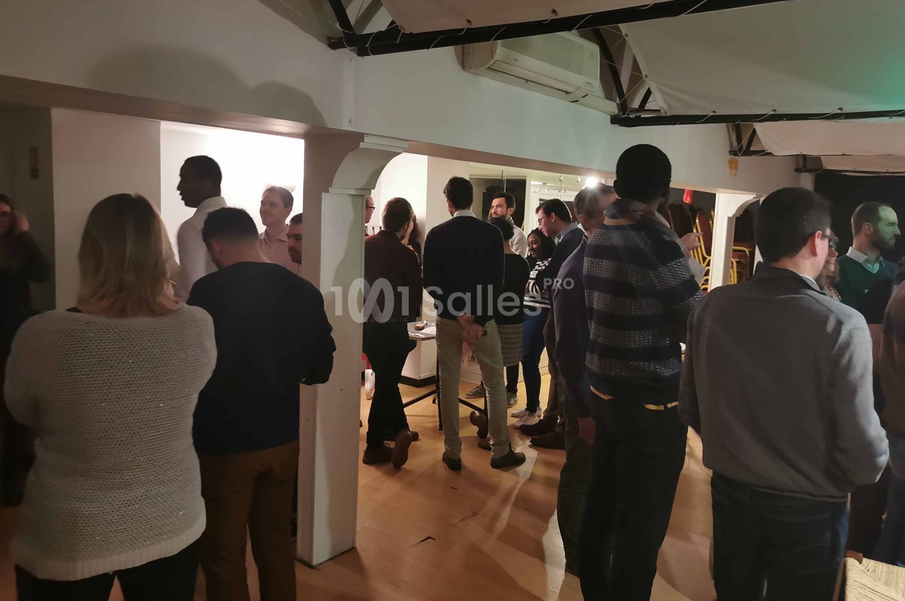 Groupe de personnes discutant dans une salle éclairée, avec des poutres apparentes et un sol en bois.