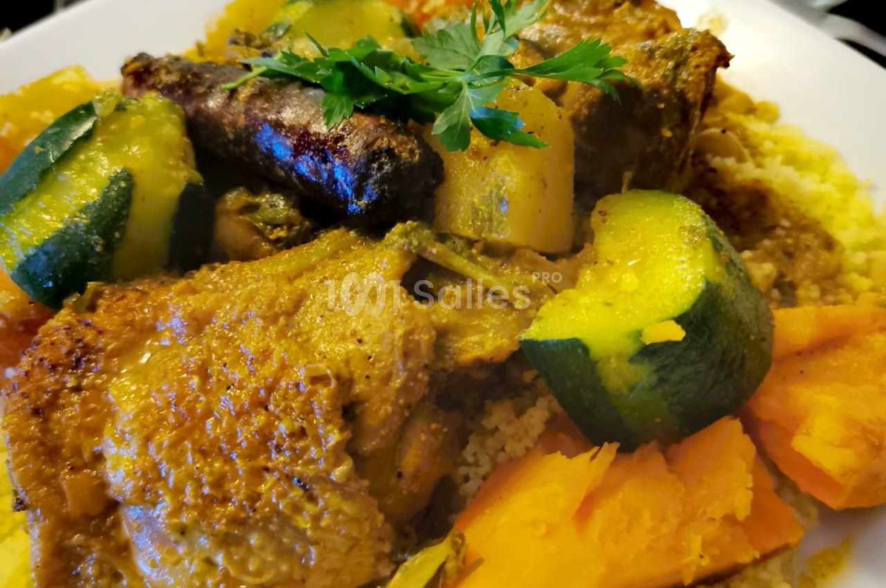 Plat de couscous avec légumes variés, morceaux de viande, merguez et herbes fraîches sur un lit de semoule.