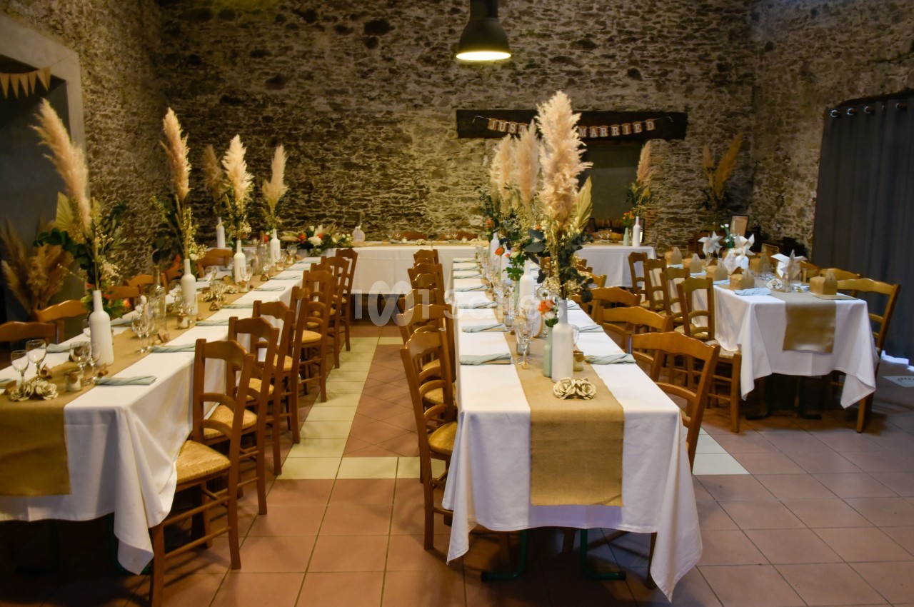 Salle de réception décorée avec des tables alignées, nappes blanches, chemins de table en toile de jute et bouquets de…