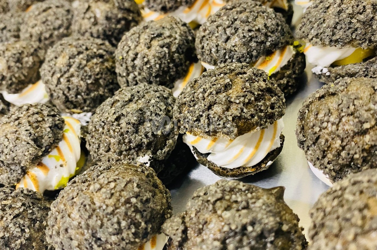 Choux noirs garnis de crème blanche et filet de caramel, disposés sur un plateau argenté.