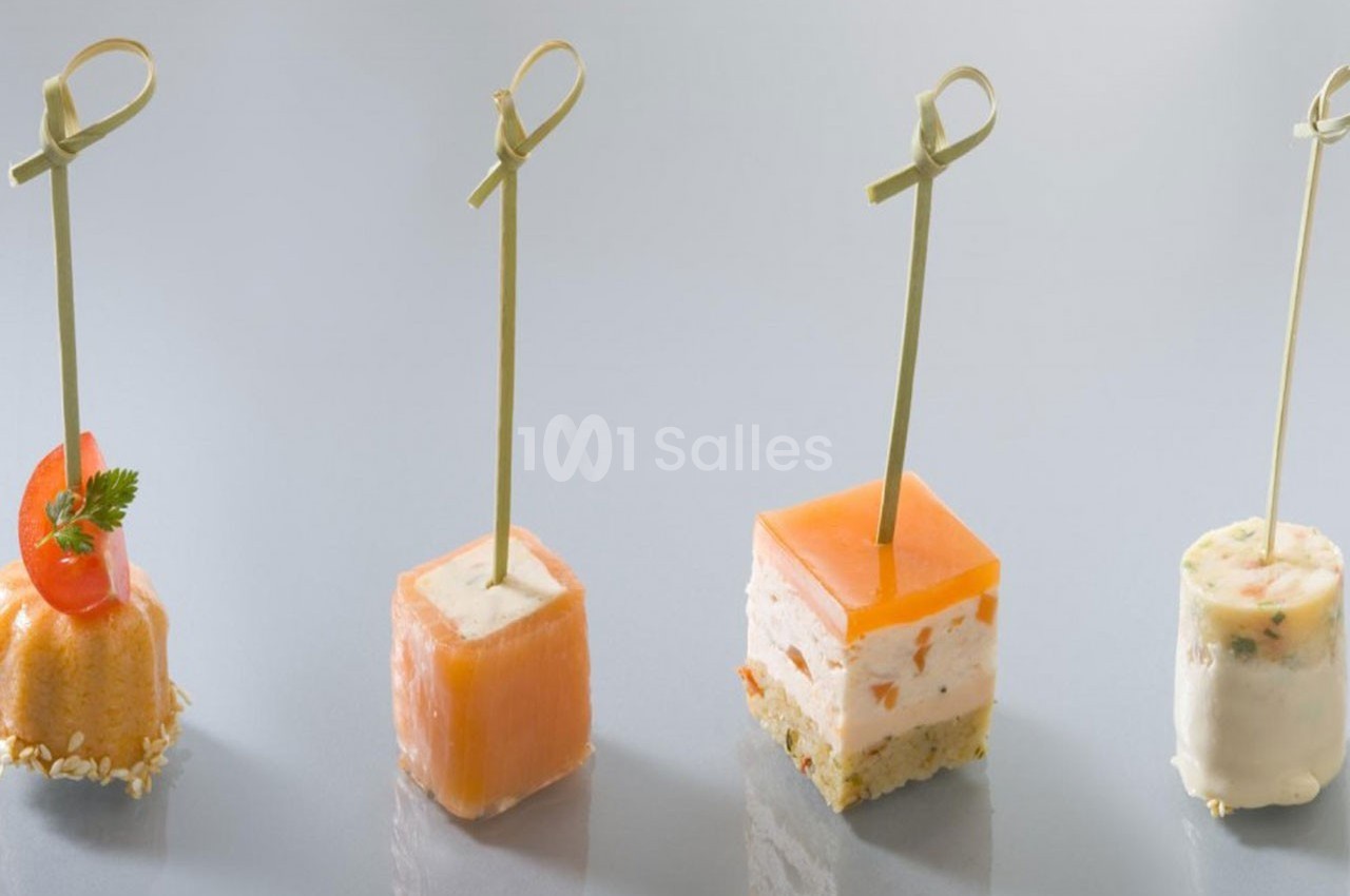Quatre amuse-bouches variés présentés sur des piques en bois, disposés sur une surface lisse et claire.