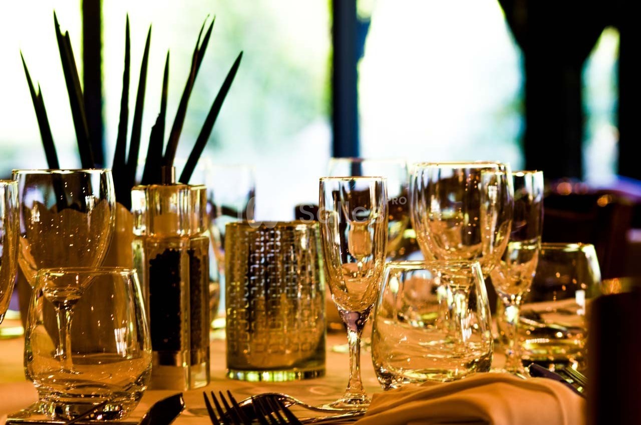 Table dressée avec des verres en cristal, une décoration végétale et un éclairage naturel en arrière-plan.