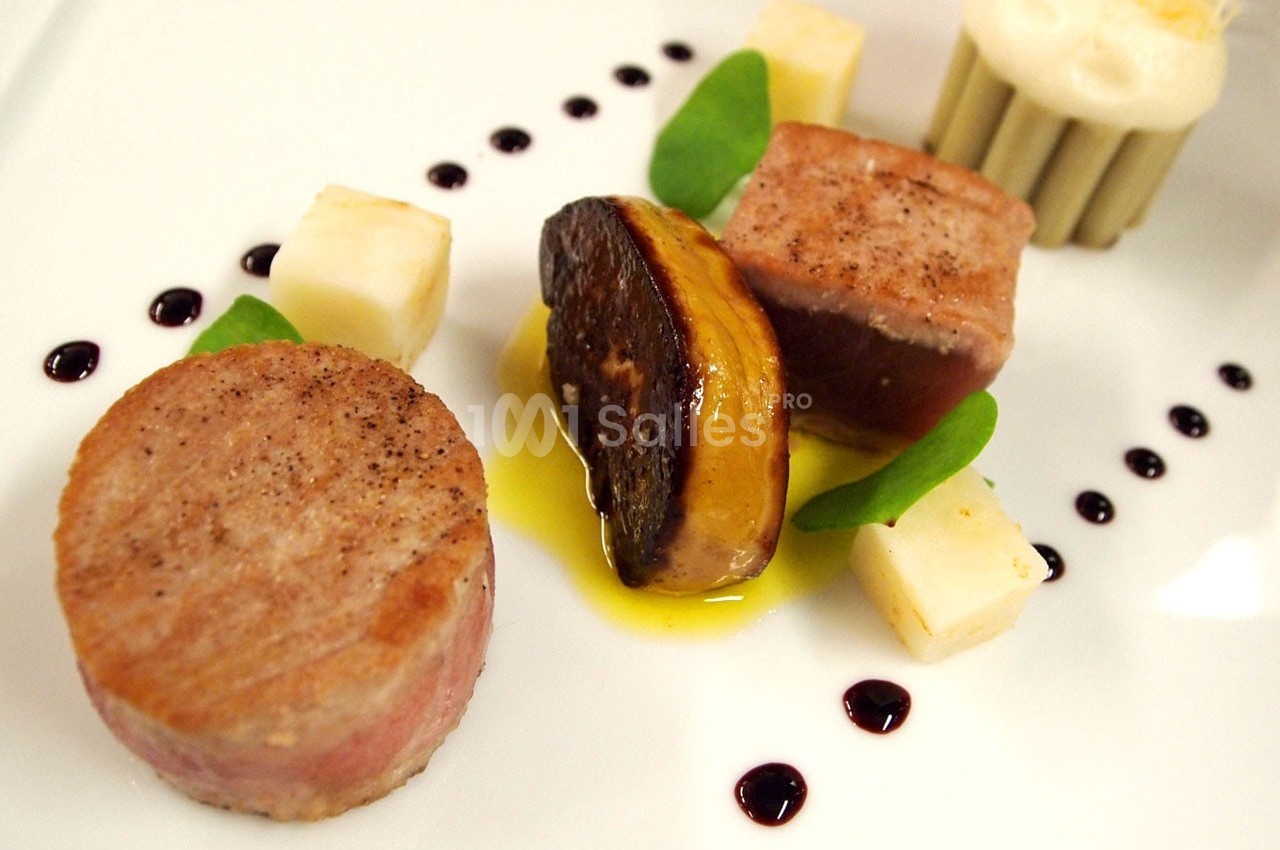 Assiette gastronomique avec viande, foie gras, cubes de fromage, sauce décorative et garniture verte.