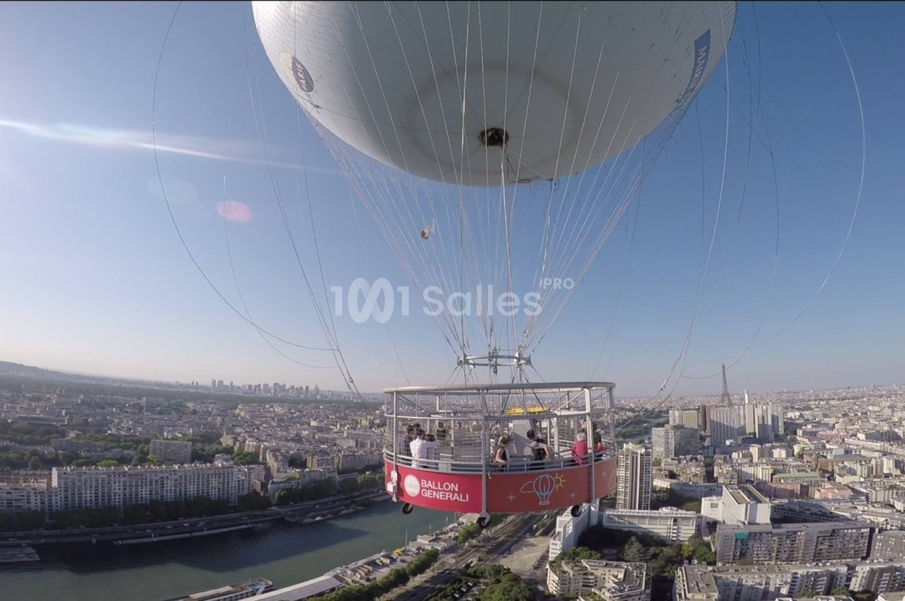 Montgolfière avec nacelle transportant des passagers survolant une ville avec une rivière et des bâtiments en arrière-plan.