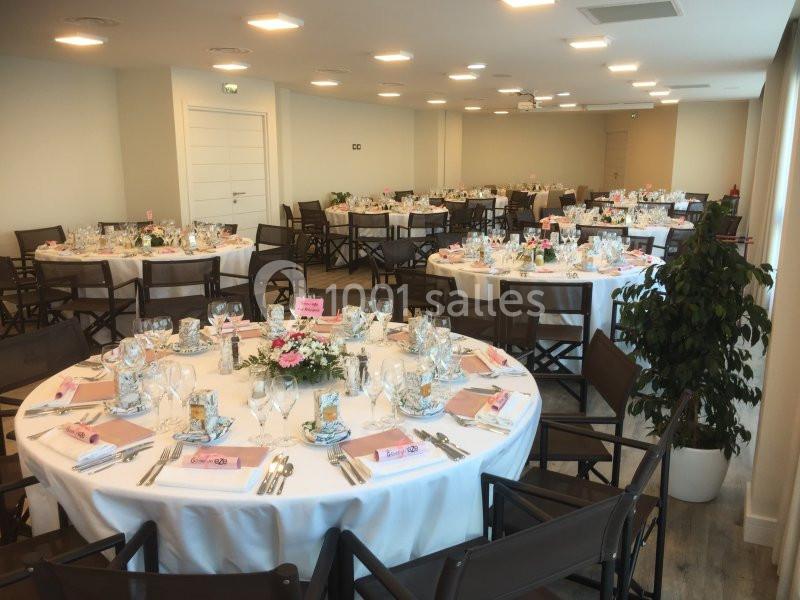 Salle de réception avec tables rondes dressées, nappes blanches, vaisselle élégante et décoration florale.