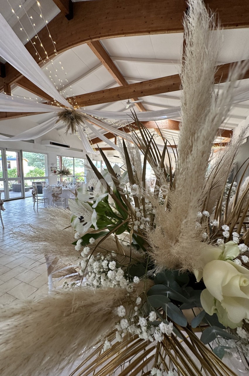 Décoration florale avec pampas, lys et gypsophile dans une salle lumineuse ornée de voilages et guirlandes.