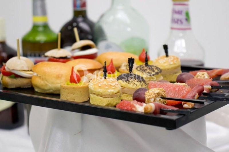 Plateau de bouchées apéritives variées avec mini-burgers, canapés et brochettes, disposé sur une table.