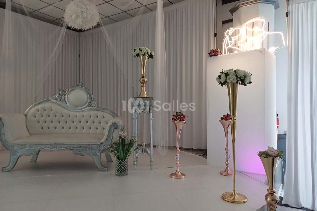 Salle décorée pour un événement avec canapé capitonné, colonnes dorées et arrangements floraux.