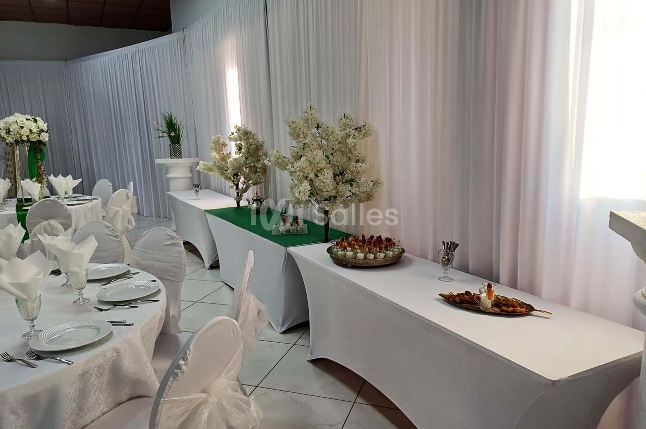 Salle de réception décorée avec des tables dressées, nappes blanches et buffets ornés de fleurs blanches.