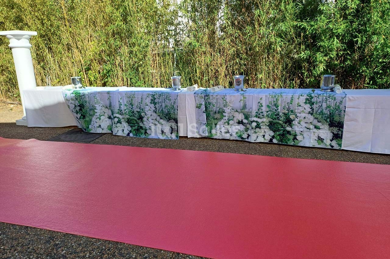 Tables décorées de nappes à motifs floraux blancs, alignées devant un tapis rouge et des bambous en arrière-plan.
