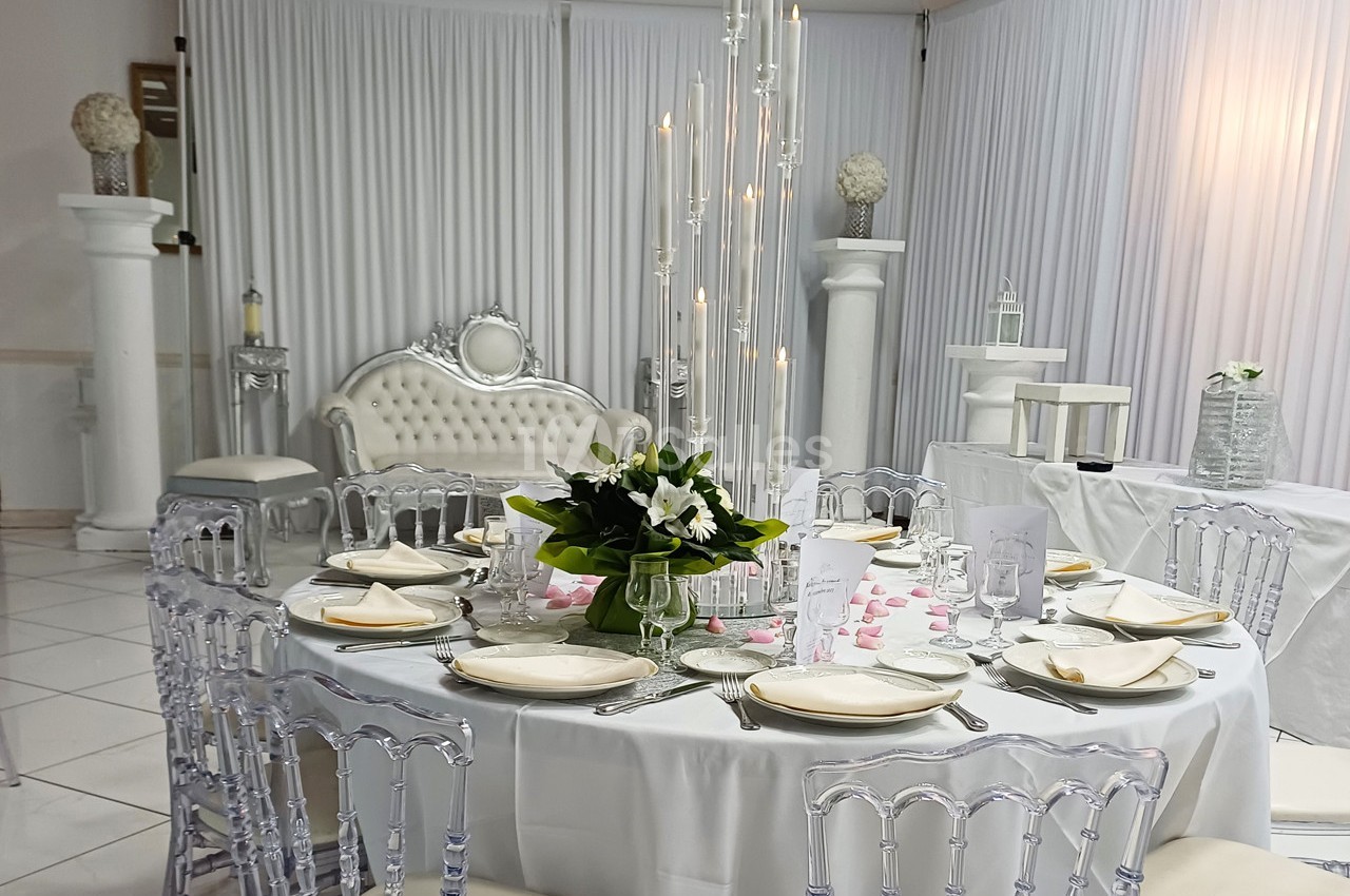Salle de réception décorée avec une table ronde élégante, des chaises transparentes et un centre de table floral.