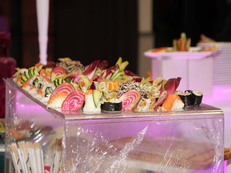 Plateau de sushis variés avec légumes colorés et garnitures, présenté sur une table éclairée par une lumière rose.