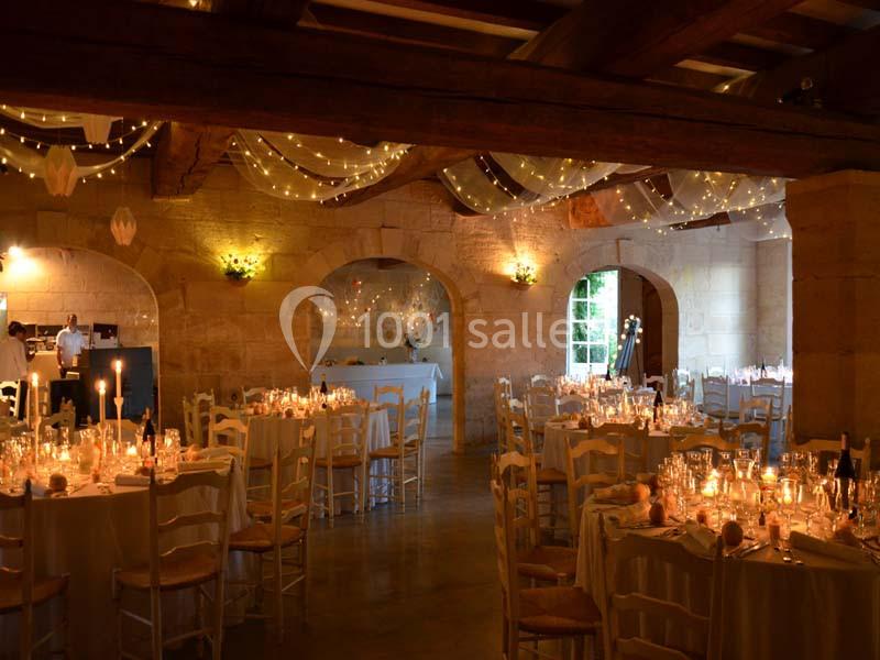 Salle de réception en pierre avec tables décorées et éclairage tamisé par des guirlandes lumineuses suspendues.