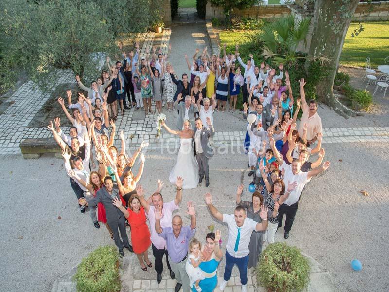Photo aérienne d'un groupe de personnes souriantes levant les bras, autour d'un couple de mariés dans un jardin.