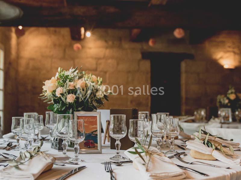 Table élégamment dressée avec vaisselle, verres, serviettes pliées et centre de table floral dans une salle en pierre.