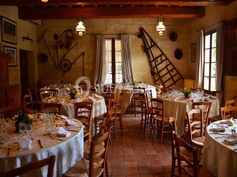 Salle de restaurant rustique avec tables rondes dressées, chaises en bois et décorations murales agricoles.