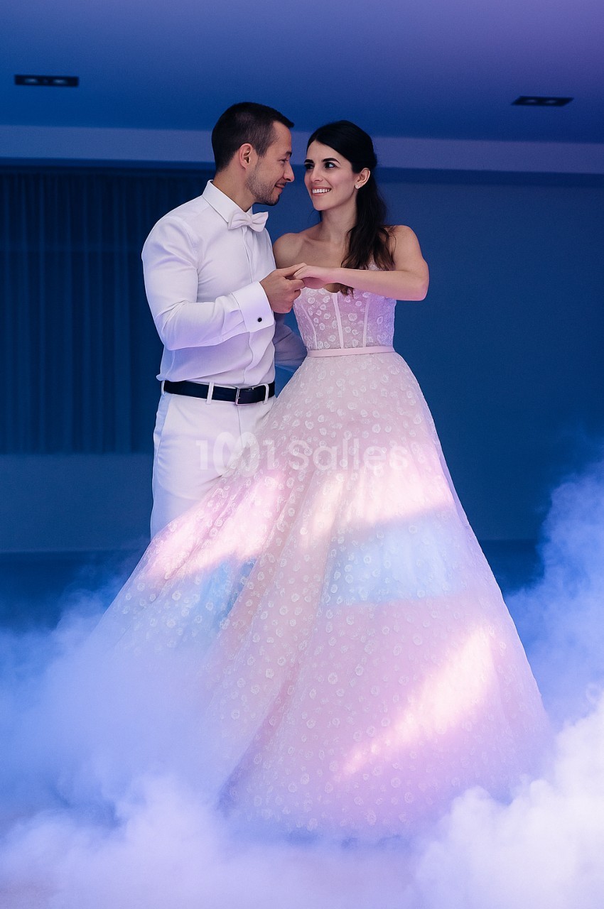 Un couple élégant danse dans une ambiance romantique avec éclairage coloré et fumée au sol.
