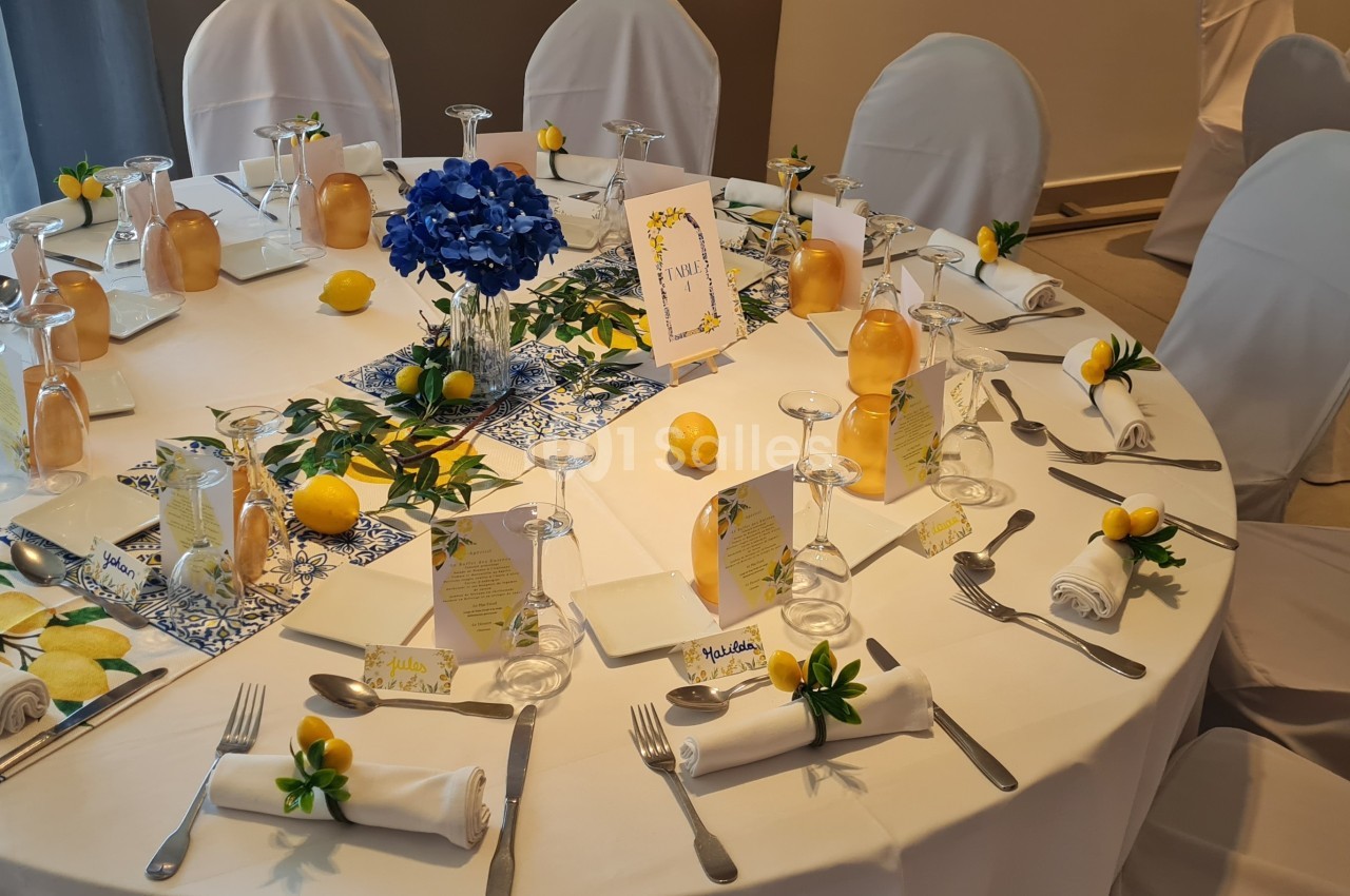 Table décorée pour un événement avec nappes blanches, citrons, fleurs bleues et menus disposés autour.