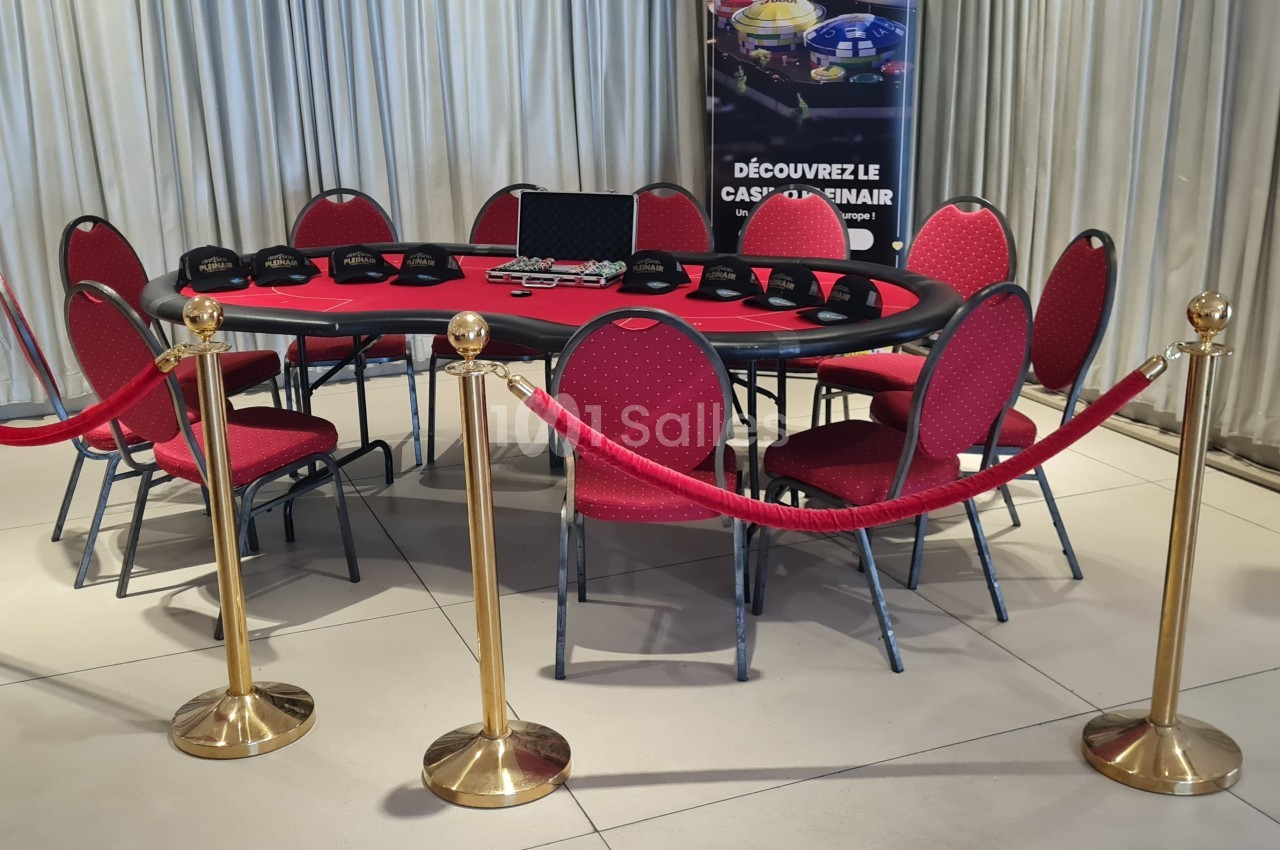 Table de poker rouge entourée de chaises, cordons de sécurité dorés et affiches en arrière-plan.
