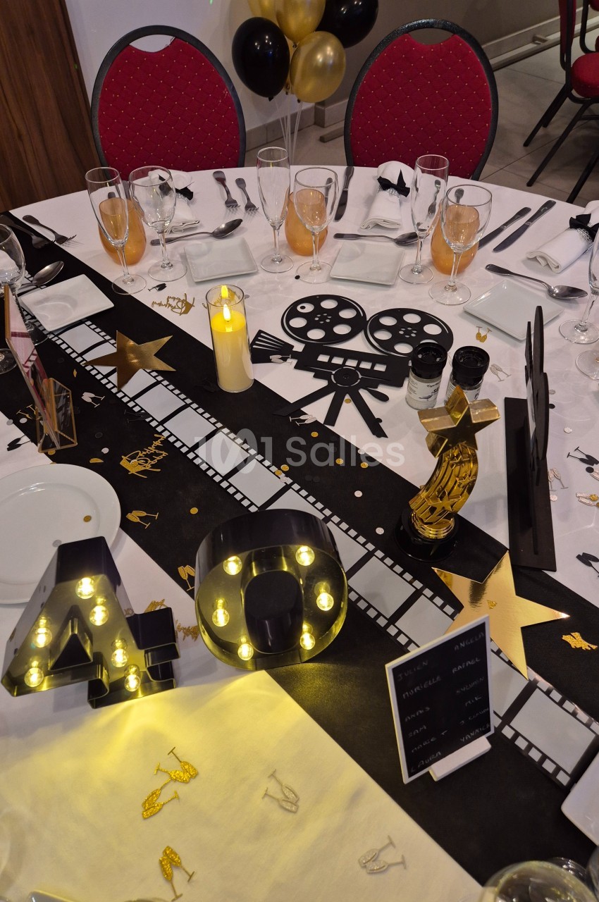 Décoration de table sur le thème du cinéma avec éléments dorés, noirs et lumineux, incluant un chiffre ’40’ éclairé.