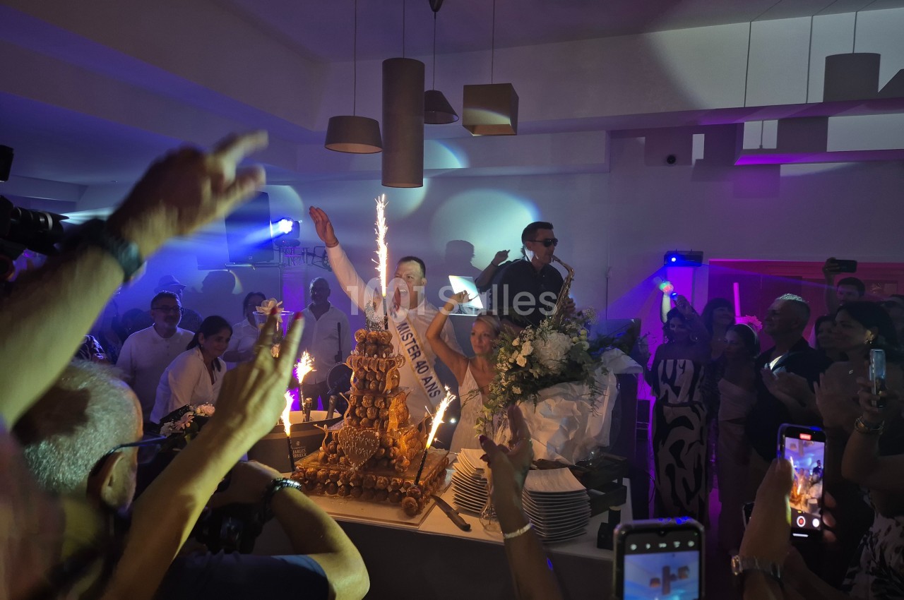 Un homme célèbre un anniversaire avec un gâteau éclairé par des bougies étincelantes, entouré d'invités festifs.