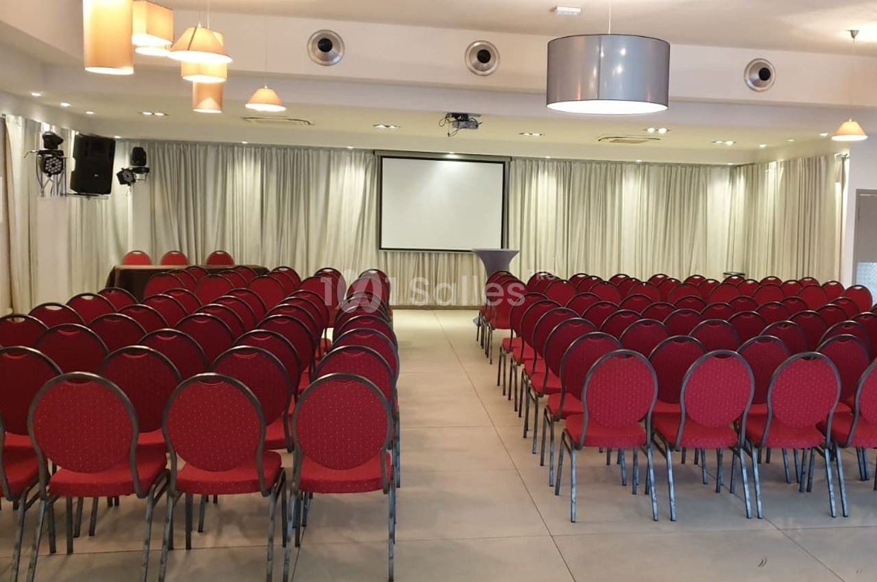 Salle de conférence avec des rangées de chaises rouges alignées face à un écran de projection.