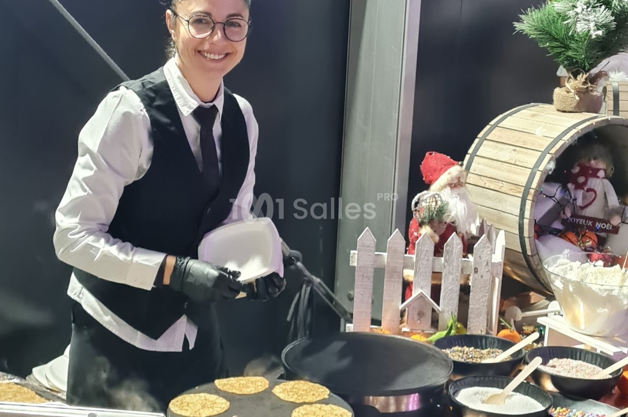 Femme souriante en tenue de service préparant des crêpes sur une plaque chauffante lors d'un événement festif.