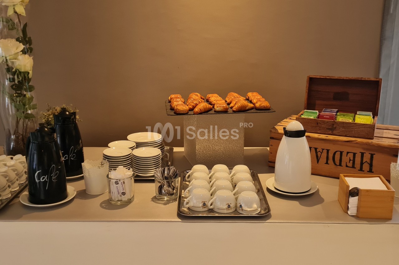 Buffet avec cafetières, tasses, viennoiseries, boîte à thé et accessoires sur une table bien organisée.