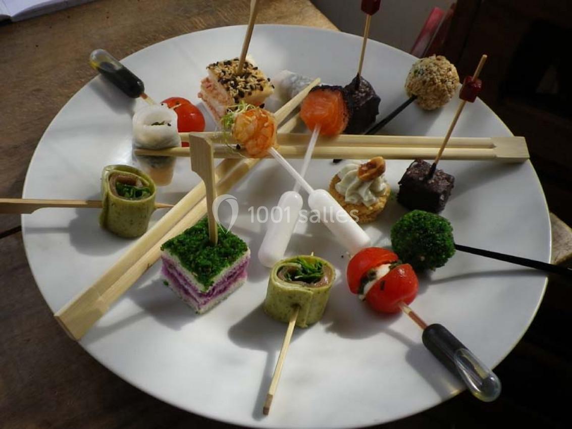 Assortiment de bouchées apéritives variées présentées sur un plateau rond, avec des brochettes et pipettes.