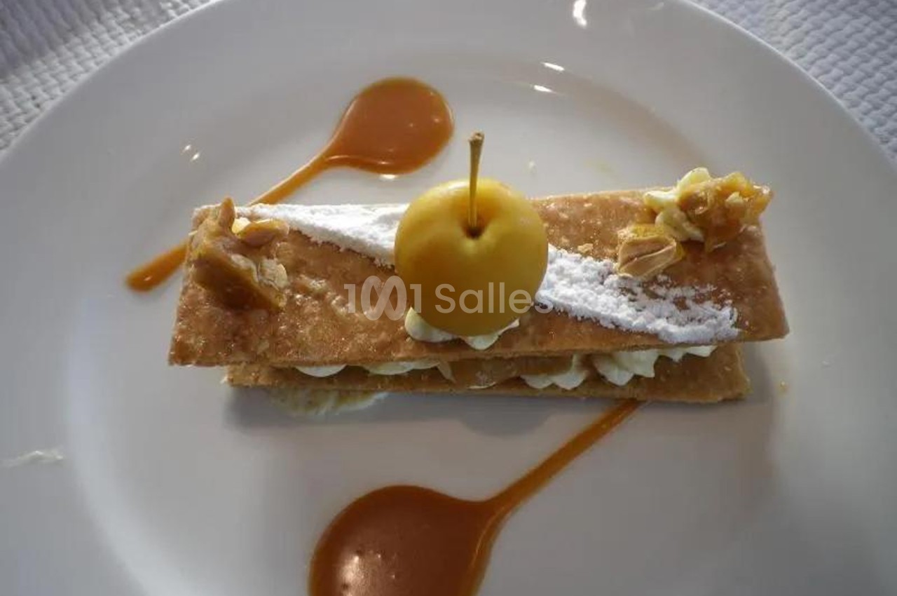 Dessert composé de couches de pâte feuilletée, crème, pomme décorative et sauce caramel sur une assiette blanche.