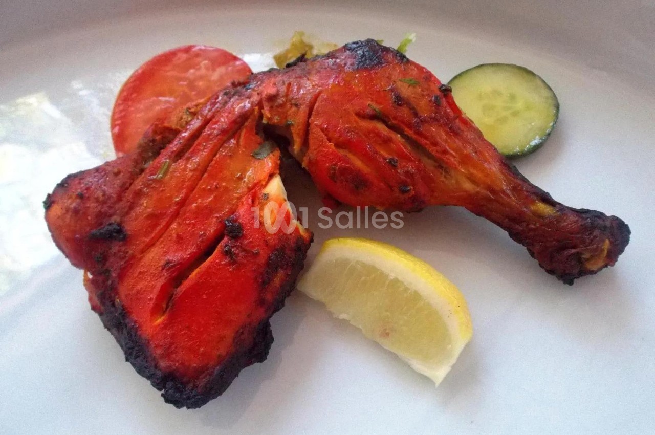 Poulet tandoori grillé servi avec une tranche de citron, une rondelle de tomate et de concombre sur une assiette blanche.