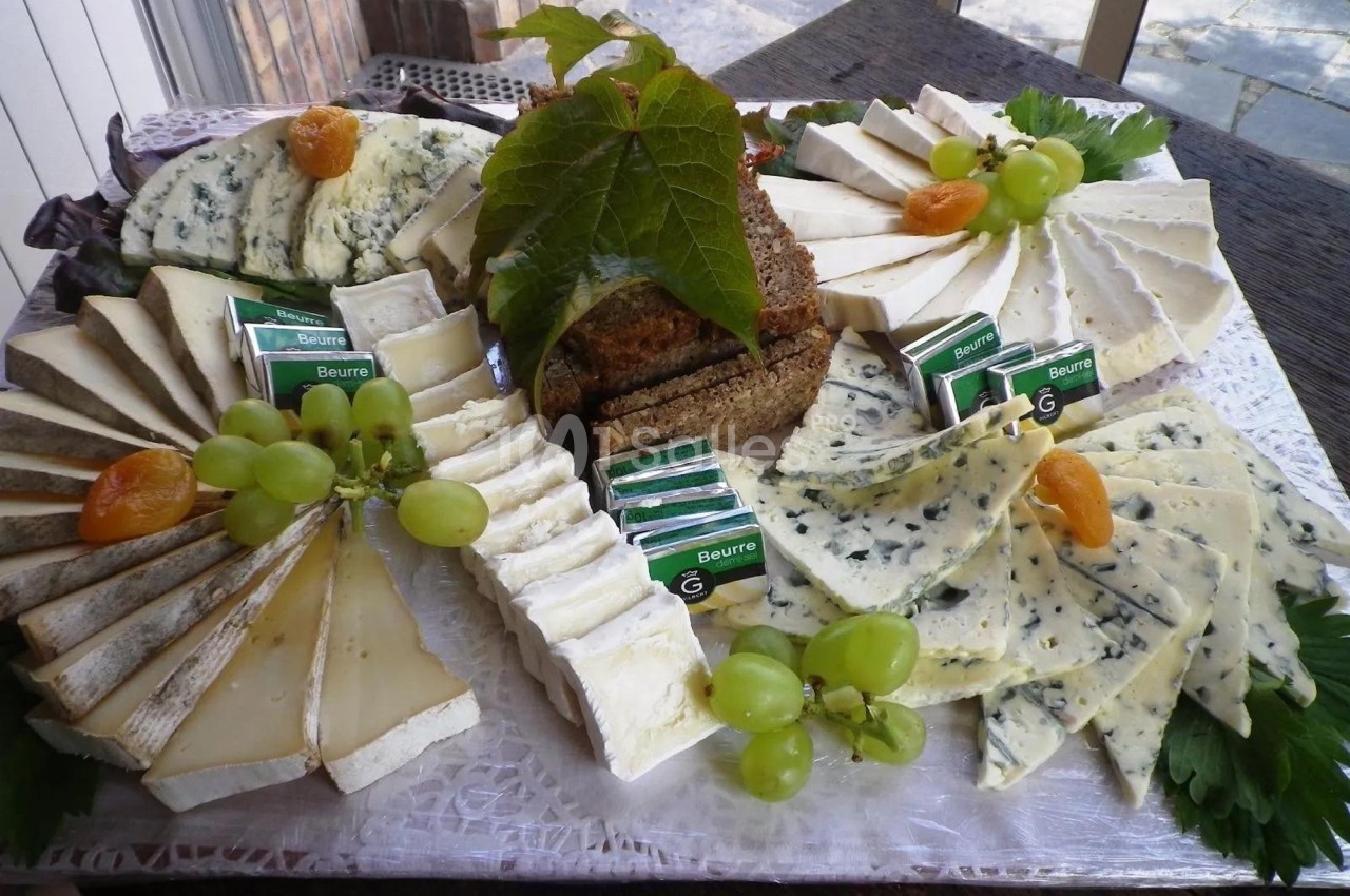 Plateau de fromages variés avec raisins, abricots secs, beurre et pain, présenté sur un plateau décoré.
