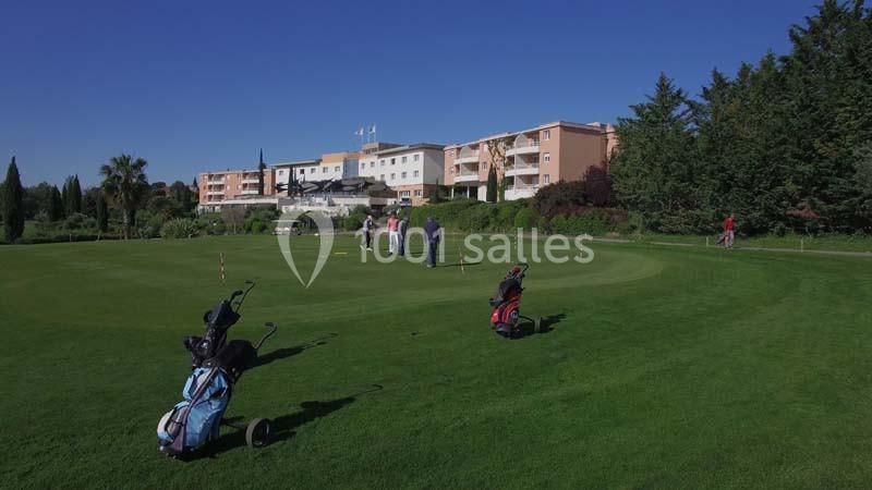Vaste terrain de golf avec sacs de clubs au premier plan et bâtiment du resort en arrière-plan sous ciel dégagé.