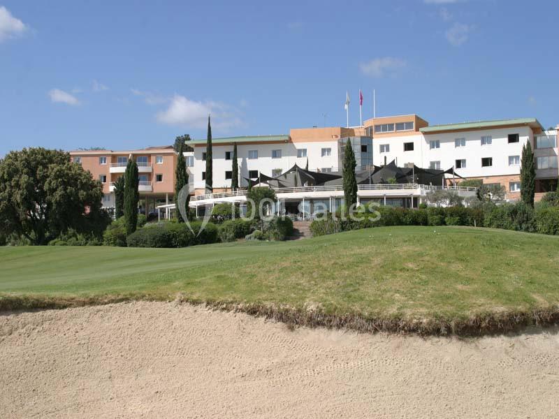 Établissement moderne en bordure d'un parcours de golf, bâtiments aux façades colorées avec terrasse et drapaux.