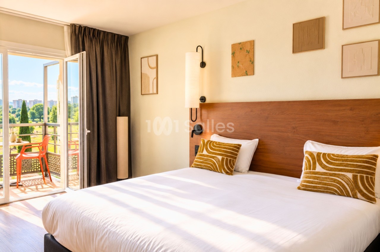 Chambre double avec lit en bois, coussins jaunes, baies vitrées ouvrant sur balcon et vue urbaine.