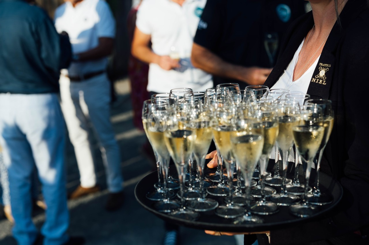 Plateau de verres de champagne tenu par une personne lors d'un événement en extérieur.
