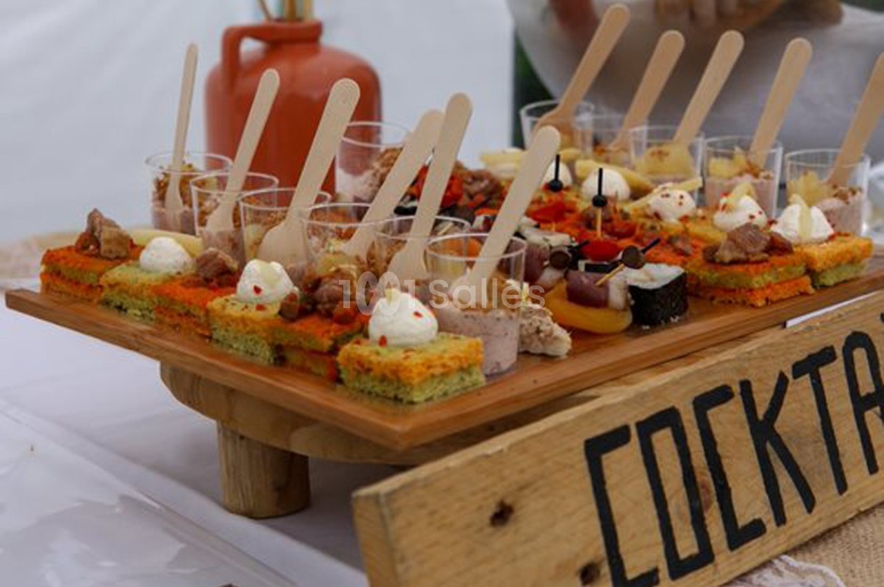 Plateau de bouchées apéritives variées présentées sur des supports en bois, avec une pancarte ’Cocktail’.
