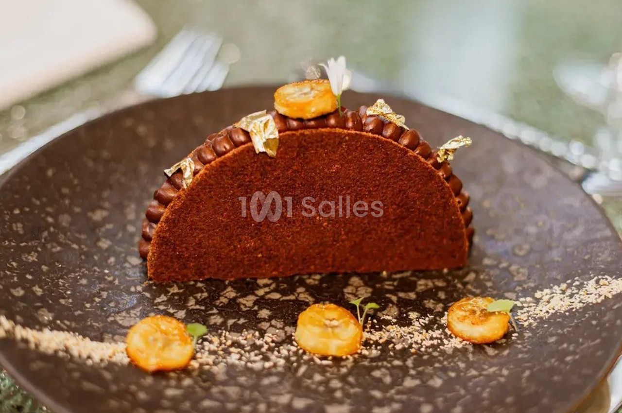 Dessert en forme de demi-lune au chocolat, décoré de bananes caramélisées, feuilles d'or et micro-pousses.