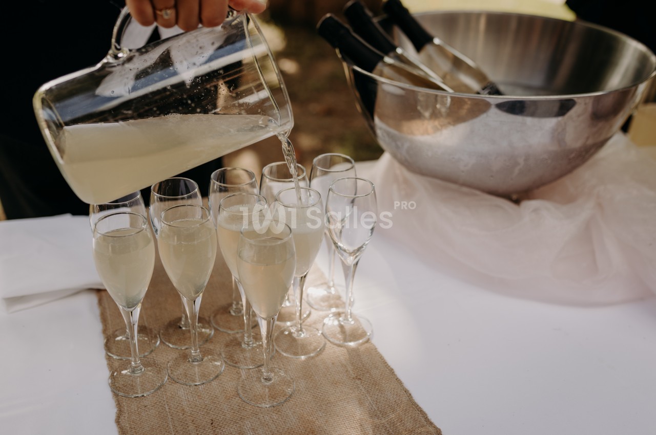 Un pichet verse une boisson pétillante dans des flûtes alignées sur une table avec un seau rempli de bouteilles.